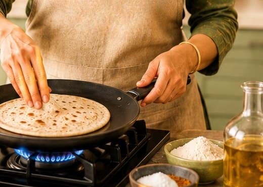 A home chef cooking a roti on a tawa over a gas flame